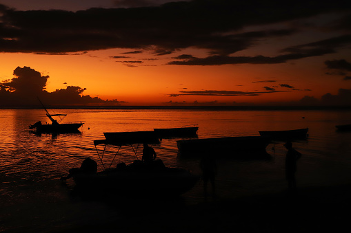 Albion, Mauritius - May 05, 2023: Vibrant colors during sunset at the Indian Ocean close the public beach with fisherman boats in Albion in the West of Mauritius. Some clouds make the scenery more spectaculor.