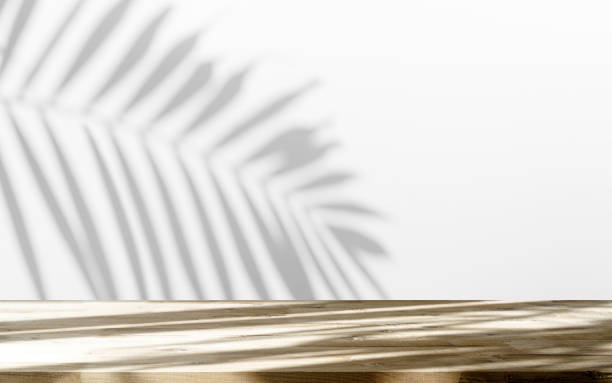 istock Table shadow background. Wooden table and white empty wall with plant shadows. 1492203677