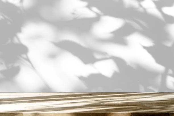 istock Table shadow background. Wooden table and white empty wall with plant shadows. 1492203785