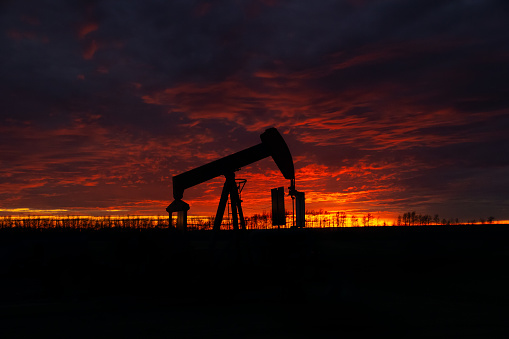 Striking orange and purple sunrise in prairies and the silhouette of an oil pump extracting fuel.