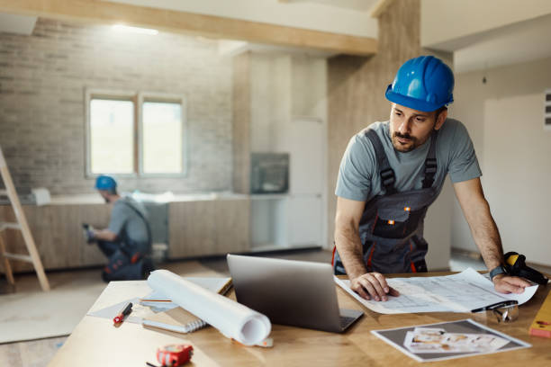 istock Worried manual worker working on laptop at renovating house. 1492207561