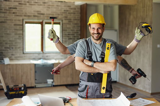 Happy multi-tasking manual worker with multiple hands working at construction site and looking at camera.