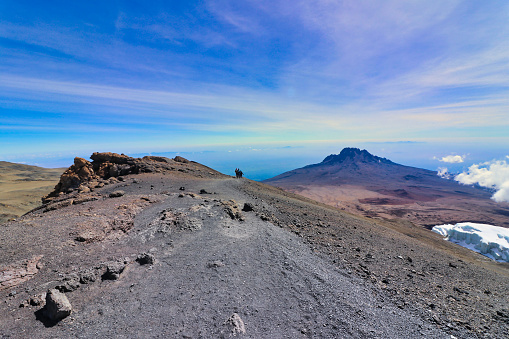 Hikers descend towards Stella Point after summiting on Kilimanjaro with Mawenzie Peak in background, Tanzania