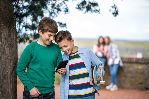 Happy teenage boys using mobile phone in public park