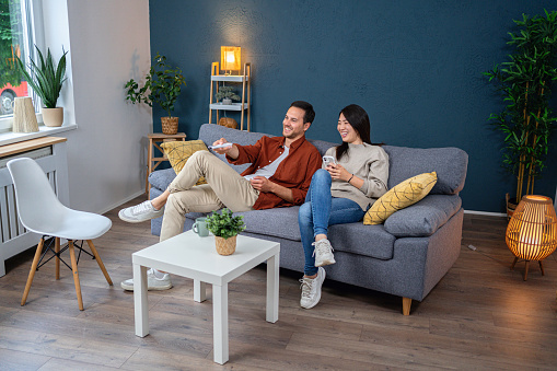 Young multiracial couple, Japanese woman and Caucasian man, sitting on the sofa in the living room and watching TV