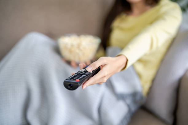 istock Asian woman Watching smart TV and using remote controller Hand holding television audio remote control at home with the remote control television 1492216047