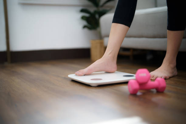 istock Fat diet and scale feet standing on electronic scales for weight control. Measurement instrument in kilogram for a diet control 1492218319
