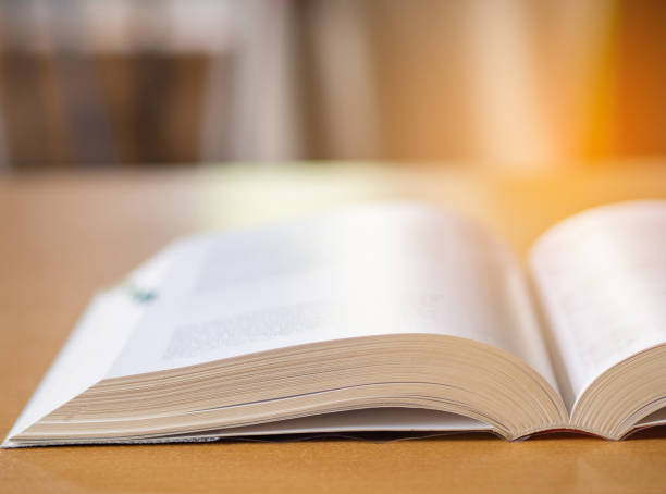 istock Close-up of open book on desk with sun light effect blur background. 1492218757