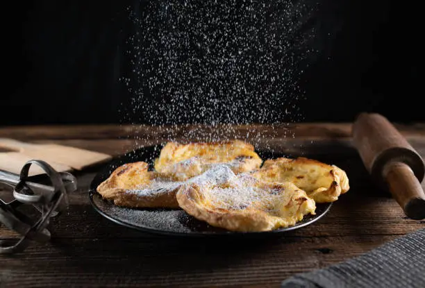 Delicious homemade baked puff pastry with sour cream, egg, lemon juice, sugar filling. Served on a platter and is sprinkling with powdered sugar on wooden table background. Closeup and front view. Freeze motion