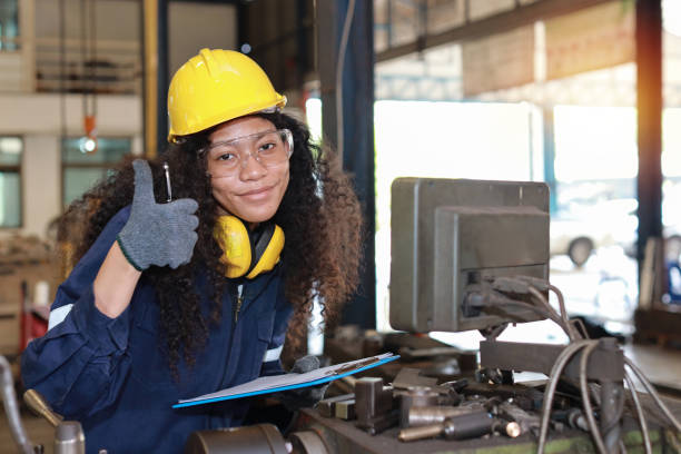 istock Technician engineer woman in protective uniform with clipboard maintenance operation or checking lathe metal machine while show thumb up at heavy industry manufacturing factory. Metalworking concept 1492221104