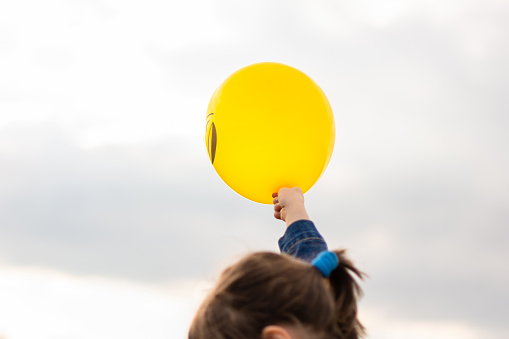 Yellow balloon in child's hand against sky