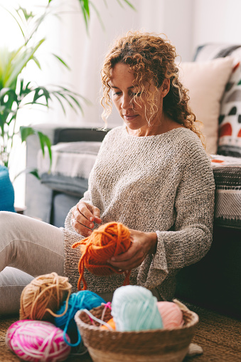 One woman having relax at home knitting working hobby sitting on the floor and enjoying handmade wool needles leisure activity indoor. Relaxation and learning new thinks. People lifestyle interior