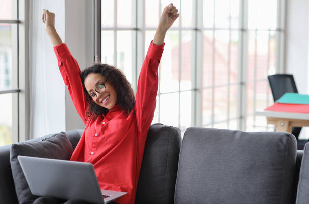 istock Happy woman sitting and using computer and raising hands with happy smiling face while shopping online in living roomBusinesswoman showing payment completed with raising hands and exciting emotion. 1492236645