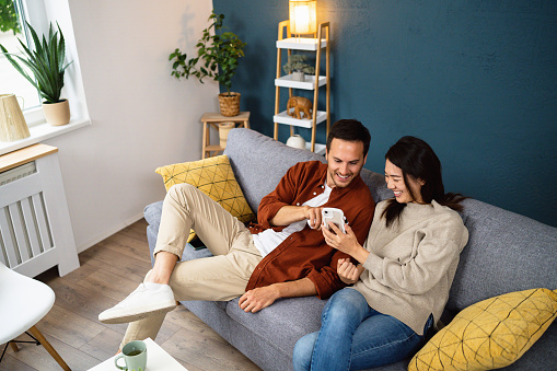 Young couple using smart phone device while relaxing on a sofa at home.