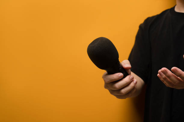 istock Hand holding microphone and towards the camera over yellow background with copy space. 1492240520