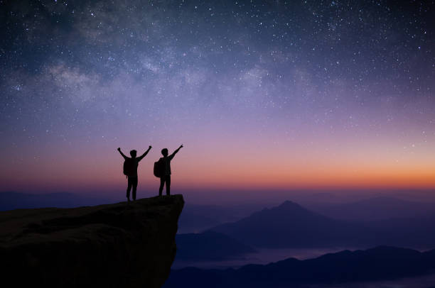 Silhouette of couple young traveler and backpacker watched the star and milky way alone on top of the mountain. He enjoyed traveling and was successful when he reached the summit. stock photo