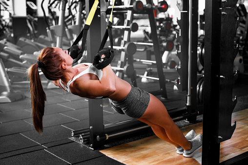 Woman doing push ups training arms with fitness straps in the gym Concept workout healthy lifestyle sport