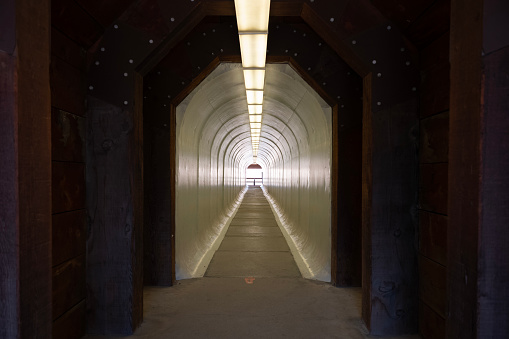 A narrow, pedestrian tunnel that is painted white and illuminated by fluorescent light fixtures sits empty.