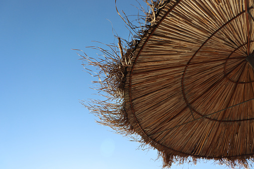 Albania. Dürres. Closeup of the straw sun umbrella on the Adriatic beach. A beautiful sunny day and the blue sky on the background.  Straw texture. Copy space. Selective focus.