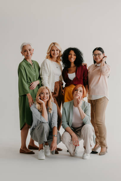 multi-ethnic group of mature women bonding and smiling against grey background - women beautiful studio shot full length imagens e fotografias de stock