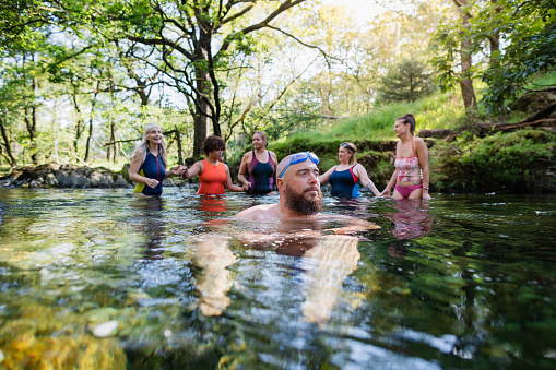Group of adults wild swimming in the Lake District, North East of England. They are in a river, enjoying time outdoors.