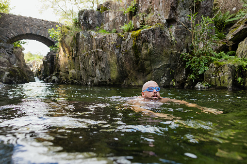 Man wild swimming in the Lake District, North East of England. He is in a river, enjoying time outdoors.