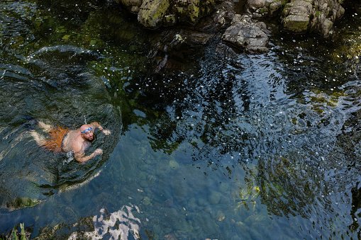 Direct above shot of a man wild swimming in the Lake District, North East of England. He is in a river, enjoying time outdoors.