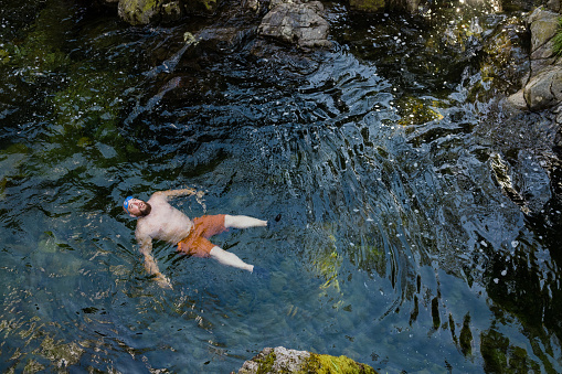 Direct above wide shot of a man wild swimming in the Lake District, North East of England. He is in a river, enjoying time outdoors.