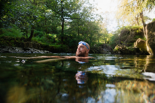 Man wild swimming in the Lake District, North East of England. He is in a river, enjoying time outdoors.