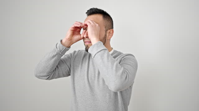 Hispanic man doing binoculars symbol with hands over isolated white background