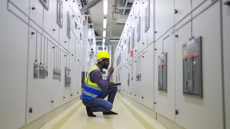 4K African man engineer working on digital tablet and talking on walkie-talkie at factory control room.