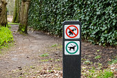 Signpost with pictograms for dogs forbidden to defecate and dogs on leash allowed on footpath in woodland, Netherlands