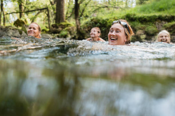 Nature Escape Group of women wild swimming in the Lake District, North West of England. They are in a river, enjoying time outdoors. woman cold water swimming stock pictures, royalty-free photos & images
