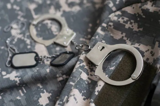 Photo of military camouflage uniform, handcuffed on background.