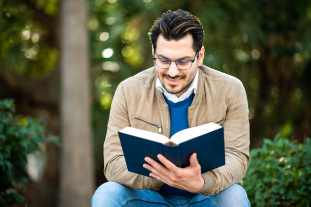 istock Male student reading a book on a bench outdoor 1492278463