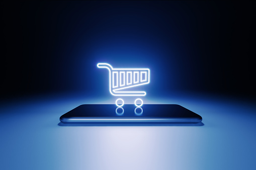 A shopping cart symbol glowing over a smart phone on blue background. Horizontal composition with copy space.
