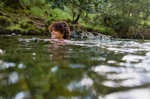 Woman wild swimming in the Lake District, North East of England. She is in a river, enjoying time outdoors.