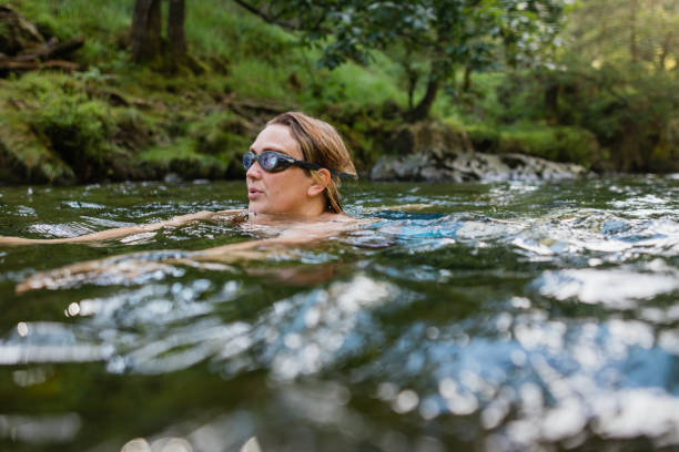 Carefree in the Water Woman wild swimming in the Lake District, North West of England. She is in a river, enjoying time outdoors, wearing goggles while she swims. woman cold water swimming stock pictures, royalty-free photos & images