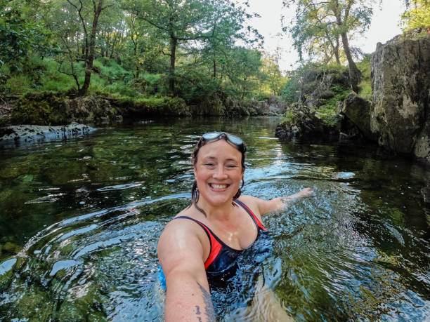 Selfie in the River Woman taking a selfie while wild swimming in the Lake District, North West of England. She is in a river, enjoying time outdoors, looking at the camera. woman cold water swimming stock pictures, royalty-free photos & images