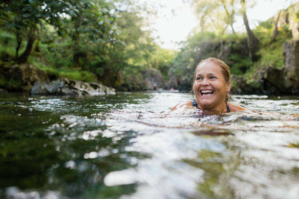 I Love the Water Woman wild swimming in the Lake District, North West of England. She is in a river, enjoying time outdoors. woman cold water swimming stock pictures, royalty-free photos & images