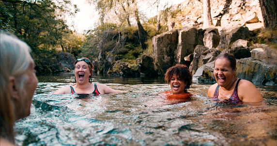 Group of women wild swimming in the Lake District, North East of England. They are in a river, enjoying time outdoors.