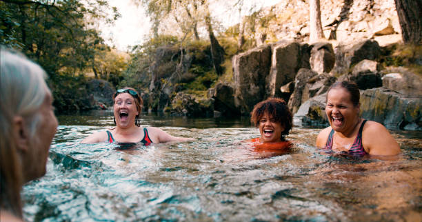 Living Actively Together Group of women wild swimming in the Lake District, North West of England. They are in a river, enjoying time outdoors. woman cold water swimming stock pictures, royalty-free photos & images