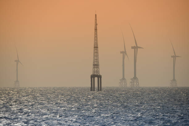 Fans of wind turbines spin over the sparkling sea. An offshore wind farm off the northwest coast of Taiwan. One of green power.