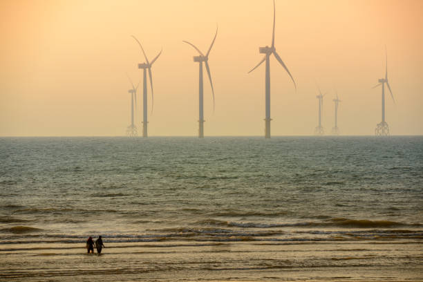 Fans of wind turbines spin over the sparkling sea. Dynamic clouds at sunset. An offshore wind farm off the northwest coast of Taiwan. One of green power.