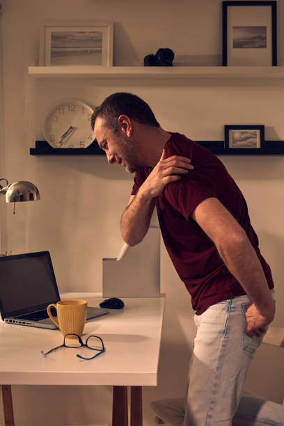 istock Man with shoulder and neck pain while working on a laptop at home. 1492283103
