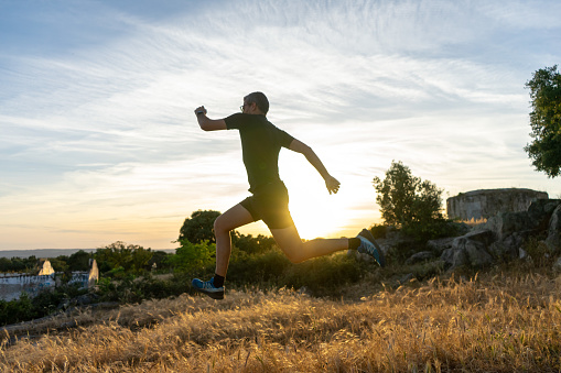 Évora, Portugal, May 22, 2023. Man with gray hair, glasses and dressed in black running clothes, doing trail running in the fields of Alentejo, almost at sunset.