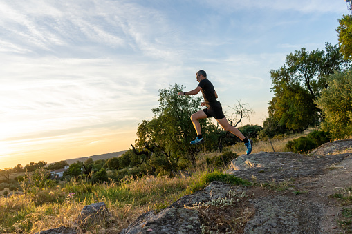 Évora, Portugal, May 22, 2023. Man with gray hair, glasses and dressed in black running clothes, doing trail running in the fields of Alentejo, almost at sunset.