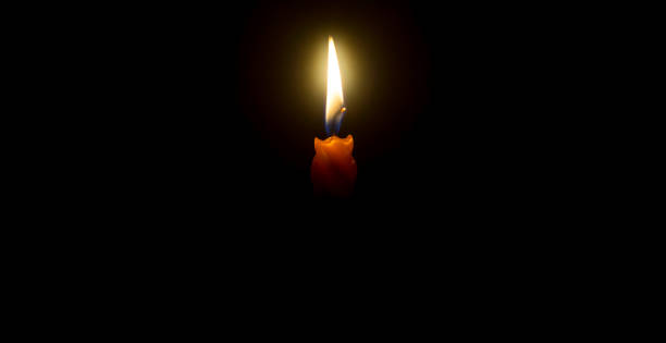 教会のテーブルの上の黒または暗い背景にオレンジ色のろうそくに輝く単一の燃えるろうそくの炎または光、クリスマス、葬儀、または追悼式、コピー用スペース - candlestick holder single object zen like decoration ストックフォトと画像
