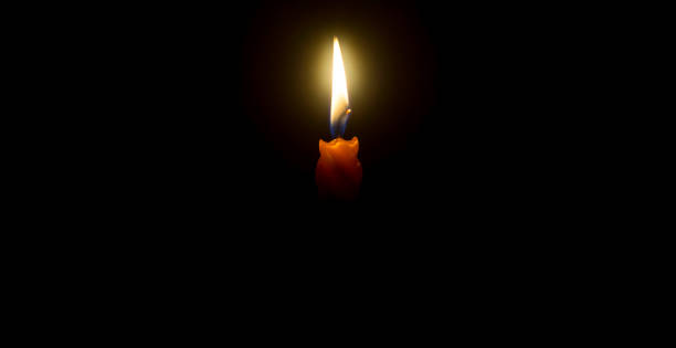 istock A single burning candle flame or light glowing on an orange candle on black or dark background on table in church for Christmas, funeral or memorial service with copy space 1492290508