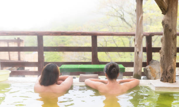 Behind view of two women enjoying views of nature while  soaking in an outdoor onsen stock photo